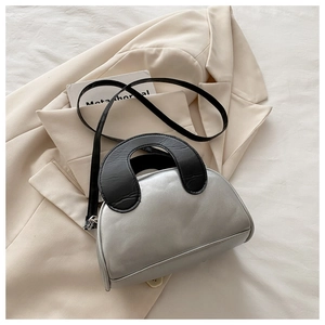 Detail of silver shell-shaped handbag with black circular handle on a white blazer