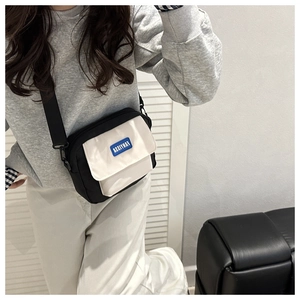 Detail of black and white contrast messenger bag with blue logo patch and wide strap
