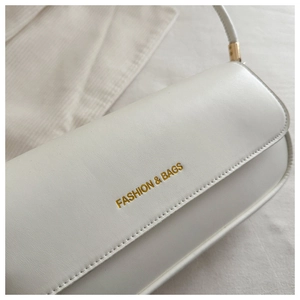 Close-up of white leather underarm bag featuring gold lettering and fine stitching details