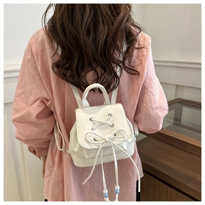 Detail of white mini backpack with decorative ribbon bow and drawstring bead charms