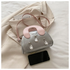 Macro shot of silver shell bag with pink strap and pearl charms next to a phone