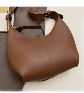 Detail of adjustable gold buckle and smooth caramel leather on moon-shaped shoulder bag