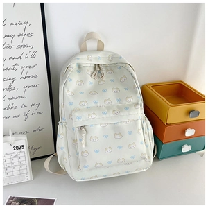 Close-up of cream backpack featuring cartoon cat patterns and blue bow details