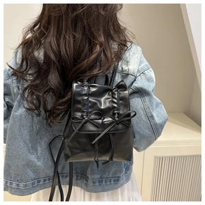 Mini black PU backpack with bow design shown on a model in a minimalist setting