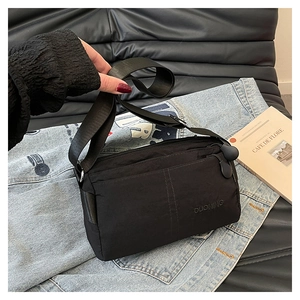 Detail of a black multi-compartment nylon crossbody bag with adjustable wide shoulder strap