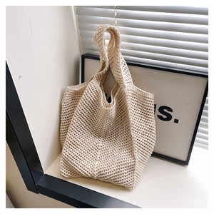 Detail of a beige crochet knit tote bag with a hollow design on a minimalist background