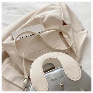 Detailed close-up of metallic silver shell bag with ivory U-handle and fashion text