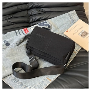 Detail of minimalist black nylon crossbody bag with logo on a leather sofa