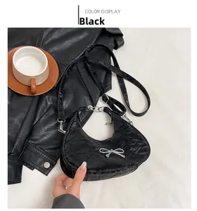 Detail of black pleated half-moon shoulder bag with a silver metal bow accent