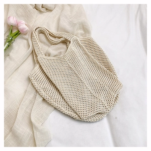 Gros plan sur un sac cabas en maille beige ajouré posé sur une literie blanche