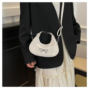 Close-up of a white crescent shoulder bag featuring a silver bow buckle on the strap