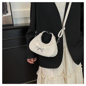 Detail of a beige half-moon crossbody bag with silver bow accent and pleated texture