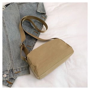 Detail of khaki nylon crossbody bag with adjustable wide fabric strap on casual denim background