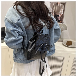 Detail of black pleated backpack with bow accents and drawstring in a minimalist setting