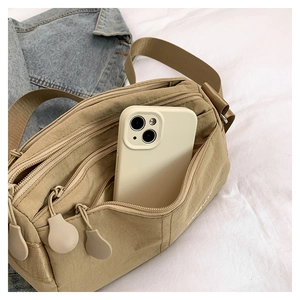 Close-up of khaki nylon crossbody bag with multi-zipper pockets and phone for size reference