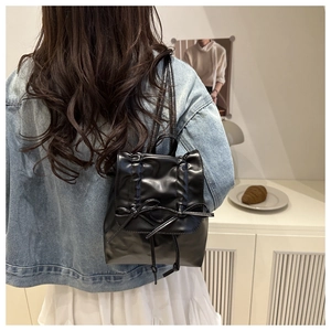 Detail of black faux leather backpack with decorative bows and ruffled edges on model