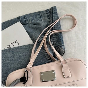 Nahaufnahme der rosa Ledertasche mit silbernem Logo-Schild und gewebtem Schlüsselanhänger