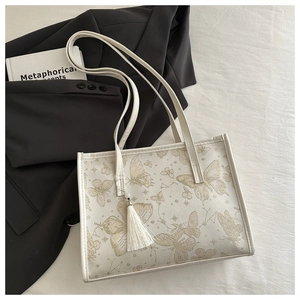 Detail der weißen Shopper-Tasche mit Schmetterlingsprint und Fransenanhänger auf Stoff