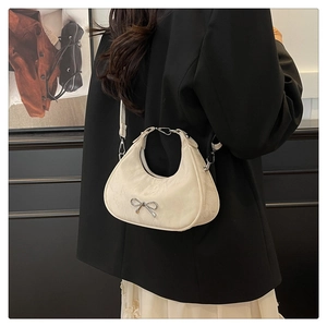 Detail of white hobo bag with silver bow accent worn by model in elegant business attire