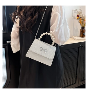 Detail of silver sequin bow handbag with pearl handle and metal chain on a model