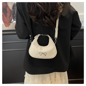 Close-up of cream bow shoulder bag on model showing crescent shape and metallic detail