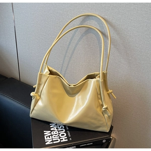 Detail of soft pleated cream yellow tote bag with slender straps on minimalist backdrop