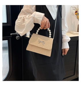 Detailaufnahme der goldenen Glitzertasche mit Perlengriff und Metallschleife