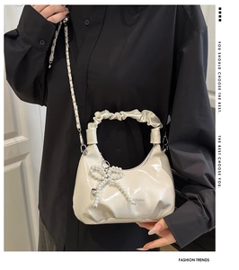 Close-up of white glossy chain bag with pleated handle and pearl bow charm detail