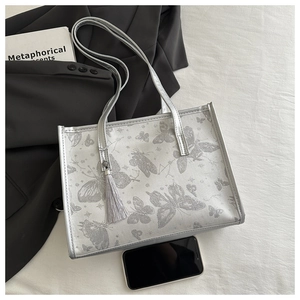 Details der silbergrauen Schmetterlings-Tasche mit Fransen-Anhänger auf stilvollem Hintergrund