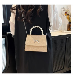 Rear view of model wearing a champagne gold glitter bag with pearl handle and silver bow