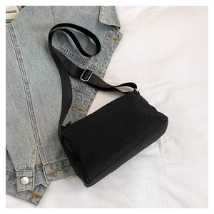 Detail view of black lightweight crossbody bag on blue denim jacket and white fabric background