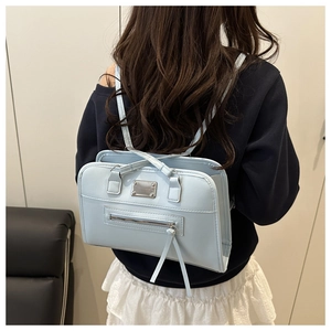 Detail eines hellblauen Kunstlederrucksacks mit Metalllogo und schmalen Schultergurten