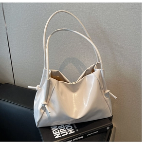 Close-up of creamy white pleated tote bag with knot strap details on a black sofa