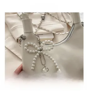Detail of white handbag featuring a pearl bow pendant and silver heart charm