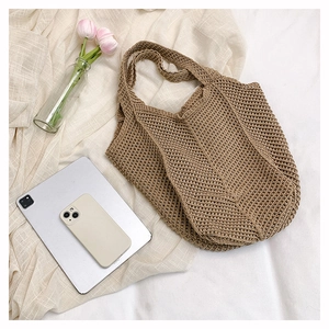 Flat lay of woven knit tote bag with tulip and tablet on beige fabric background
