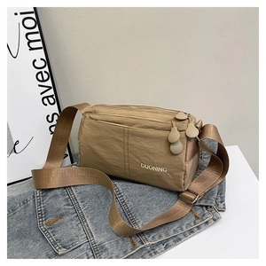 Close-up of tan nylon crossbody bag with multi-zipper layers and wide shoulder strap