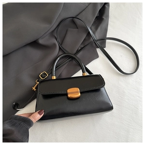 Detail of a black leather crossbody bag featuring a golden lock on textured fabric