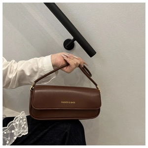 Close-up of a brown leather baguette bag with gold FASHION & BAGS lettering detail