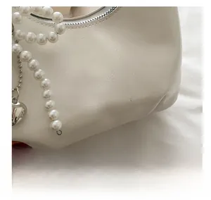 Close-up of white textured leather bag featuring pearl beads and silver heart pendant
