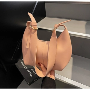 Close-up of a pink crescent hobo bag with gold hardware on a decorative book background