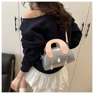 Silver shell crossbody bag with pink handle and pearl charms worn by a model