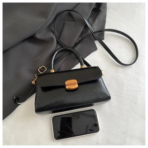Detailed view of mini black glossy leather bag with gold buckle and smartphone for scale
