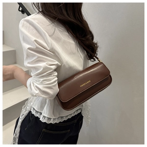 Detailed view of deep brown leather underarm baguette bag with gold lettering on a model