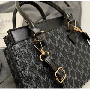 Nahaufnahme der schwarzen Tasche mit Lychee-Textur, M-Muster und goldenen Beschlägen