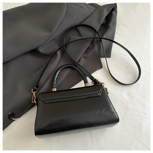 Detail of a black glossy leather mini bag with gold hardware on white and grey textures