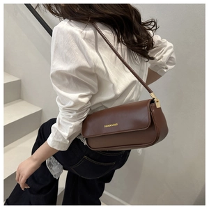 Detail of a brown leather shoulder bag with yellow text on a minimal studio background