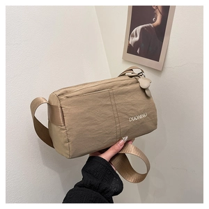 Detail of khaki pleated crossbody bag featuring a white DUONING logo and wide strap