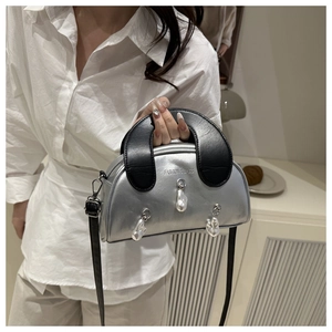 Detailed view of silver shell bag featuring decorative pearls and black leather handle