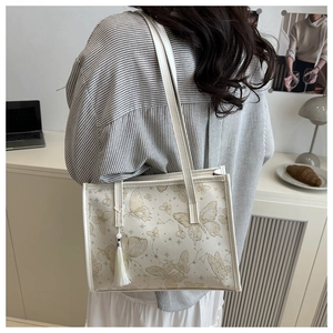 Detail der weißen Shopper-Tasche mit Goldstickerei und weißem Seidenquasten-Anhänger