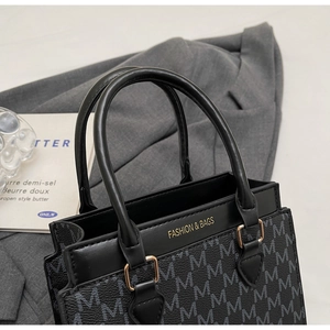 Detail der schwarzen quadratischen Tasche mit M-Print und goldener Schnalle auf grauem Blazer